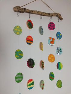 a group of different colored eggs hanging from a wooden stick on a wall next to a white wall