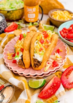 two tacos are sitting on a pink plate next to some salad and condiments