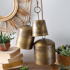 three bells hanging from the side of a wall next to books and succulents