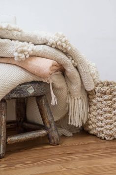 a pile of blankets sitting on top of a wooden bench next to a basket and blanket