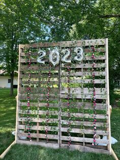 a sign made out of wooden pallets with flowers and numbers on the side, in front of some trees