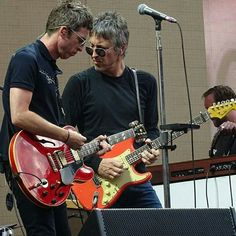 two men standing next to each other while playing guitars