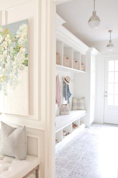 a white entryway with a bench, coat rack and paintings hanging on the wall