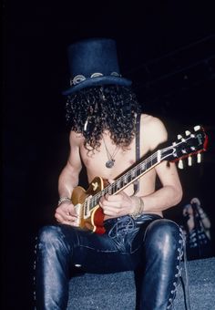 a man sitting on the ground with a guitar in his hand and wearing a top hat