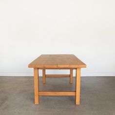 a wooden table sitting on top of a cement floor in front of a white wall