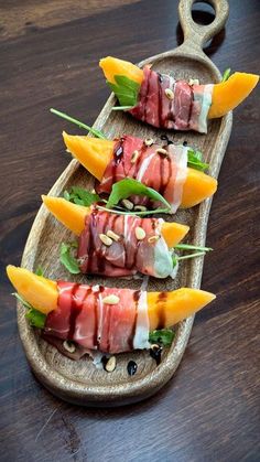 four pieces of sushi on a wooden platter with green garnish and mango slices