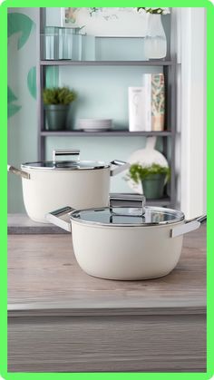 two white pans sitting on top of a wooden table next to a green shelf