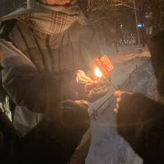 two people holding a lit candle in their hands while standing on the snow covered ground