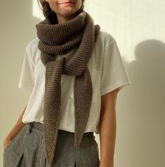 a woman standing in front of a white wall wearing a brown knitted scarf over her neck