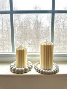 two white candles sitting on top of a window sill