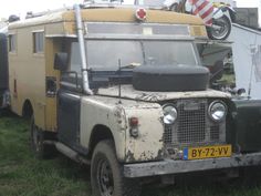 an old truck is parked in the grass with other vehicles behind it and people standing around