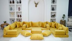 a living room filled with lots of yellow couches and pillows on top of a white rug