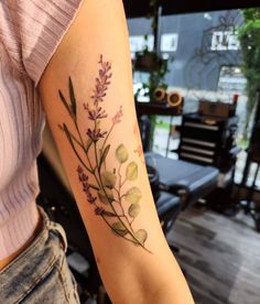 a woman with a tattoo on her arm that has purple flowers and leaves growing out of it