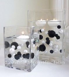 two clear square vases with black and white balls in the center, one filled with candles