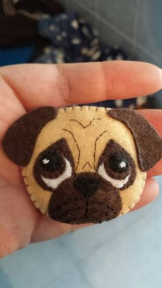 a hand holding a small brown and white dog brooch with eyes on it's face