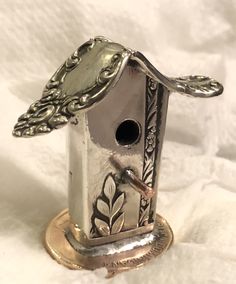 a silver birdhouse sitting on top of a gold plate