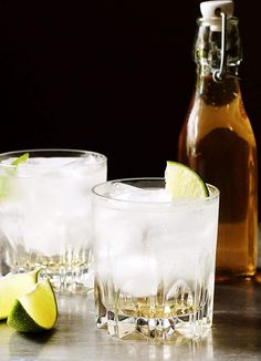 two glasses filled with ice and limes next to a bottle