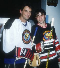 two men standing next to each other holding hockey sticks and gloves in their hands,