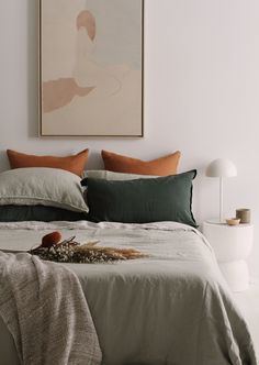 a bed with pillows and blankets on top of it in front of a framed painting