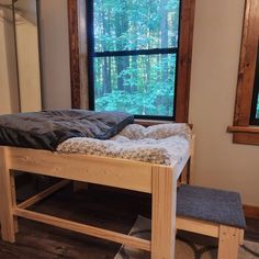 a bed sitting in front of a window next to a wooden bench with a blanket on it