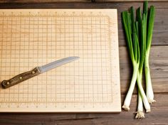 green onions are on a cutting board next to a knife and scallion stalks