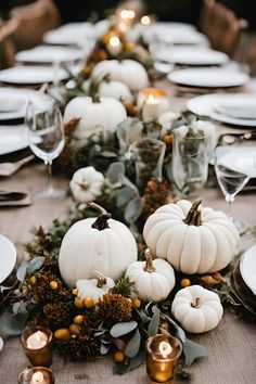 a long table with white pumpkins and greenery on it, surrounded by candles