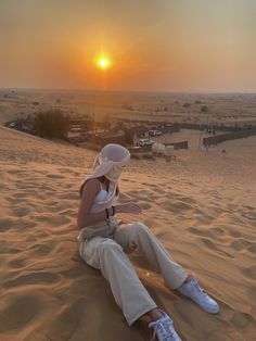 a woman sitting on top of a sandy beach next to the sun in the sky