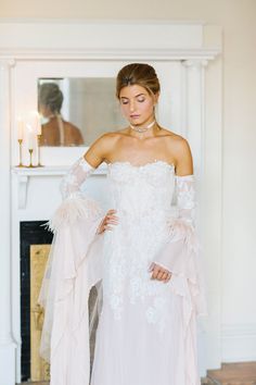 a woman in a white wedding dress standing next to a fireplace with her hands on her hips