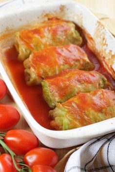 stuffed cabbage and tomatoes in a white dish on a wooden table next to fresh cherry tomatoes