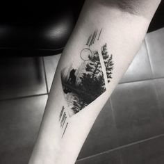 a person with a tattoo on their arm is standing in front of a mountain and trees