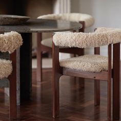 a table with two chairs that have sheepskin seats on them, and one chair is upholstered at the end