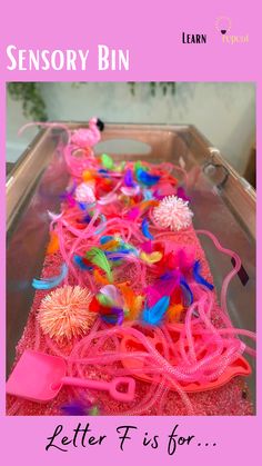 a pink plastic tray filled with lots of different colored items and text that reads, sensory bin