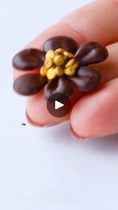 a hand holding a tiny flower made out of chocolate and yellow beads on it's thumb