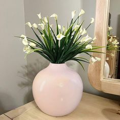 a pink vase filled with white flowers on top of a wooden table next to a mirror