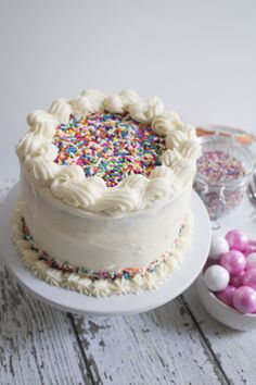 a white cake with sprinkles on it sitting next to some candies