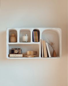 a shelf filled with books and other items on top of a white wall next to a window