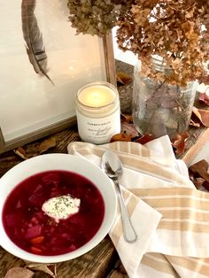 a bowl of soup on a table next to a candle and some autumn leaves in the background