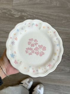 a person holding a white plate with pink and blue flowers on it, in front of a wood floor