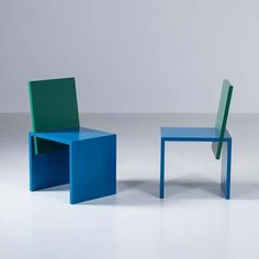 two blue and green chairs sitting next to each other on a white floor in front of a gray wall