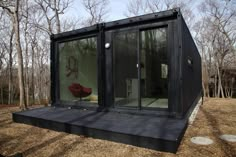 a small black container house in the woods