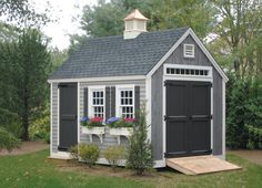 a small gray and white shed with flowers in the window boxes on the front door