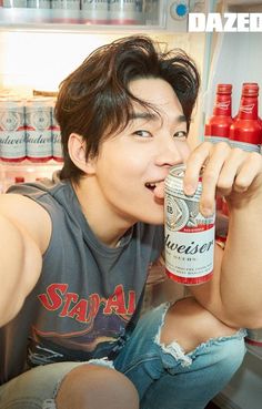 a young man is drinking from a bottle in front of an open refrigerator full of soda