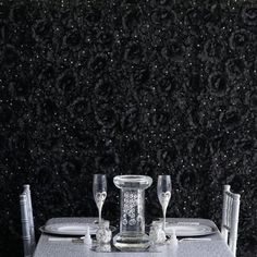 the table is set for two with silverware and wine glasses on it in front of a black wall