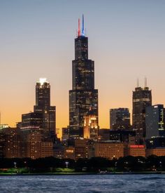 the city skyline is lit up at night, with skyscrapers in the foreground