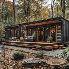 a small cabin in the woods surrounded by trees and leaves, with an outdoor seating area