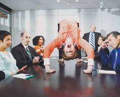 a woman is upside down in an office meeting room with other people looking at her