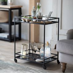 a bar cart with drinks and glasses on it in a living room next to a couch