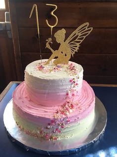 a three tiered cake decorated with pink and white frosting, topped with a fairy figurine