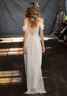 a woman walking down a runway wearing a white dress with long sleeves and flowers in her hair