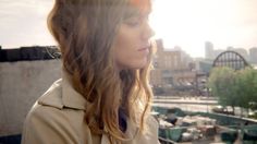 a woman with long hair standing in front of a cityscape and looking off into the distance